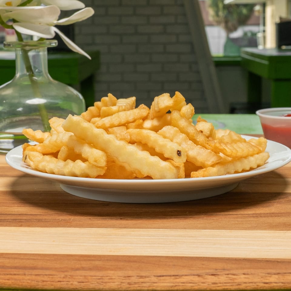 Golden crinkle-cut fries on a white plate with a cup of ketchup.