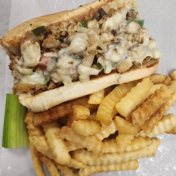 Cheesesteak sandwich with melted cheese, peppers, and onions, served with crinkle-cut fries and celery.