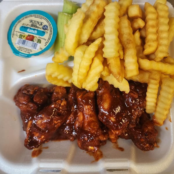 BBQ chicken wings, crinkle-cut fries, celery sticks, and a ranch dressing cup in a takeout container.